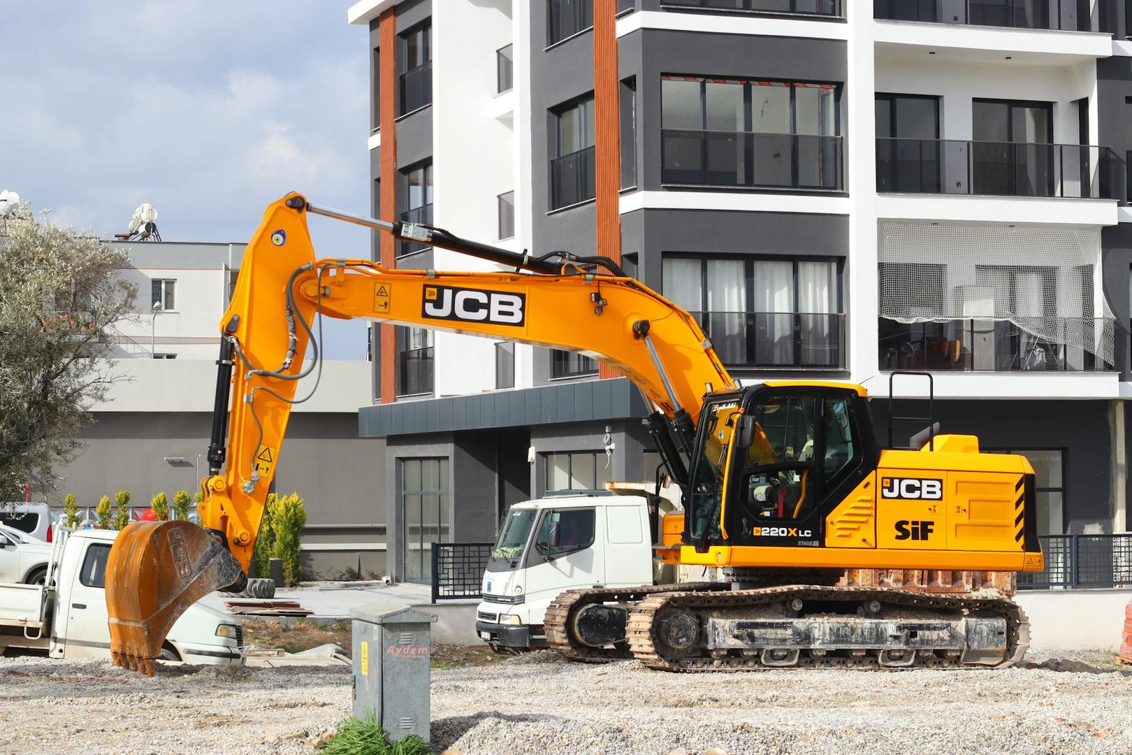 En gul JCB 220X LC grävmaskin på en byggarbetsplats nära bostadshus.
