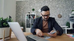 Affärsman räknar kontanter vid skrivbord med en laptop och papper